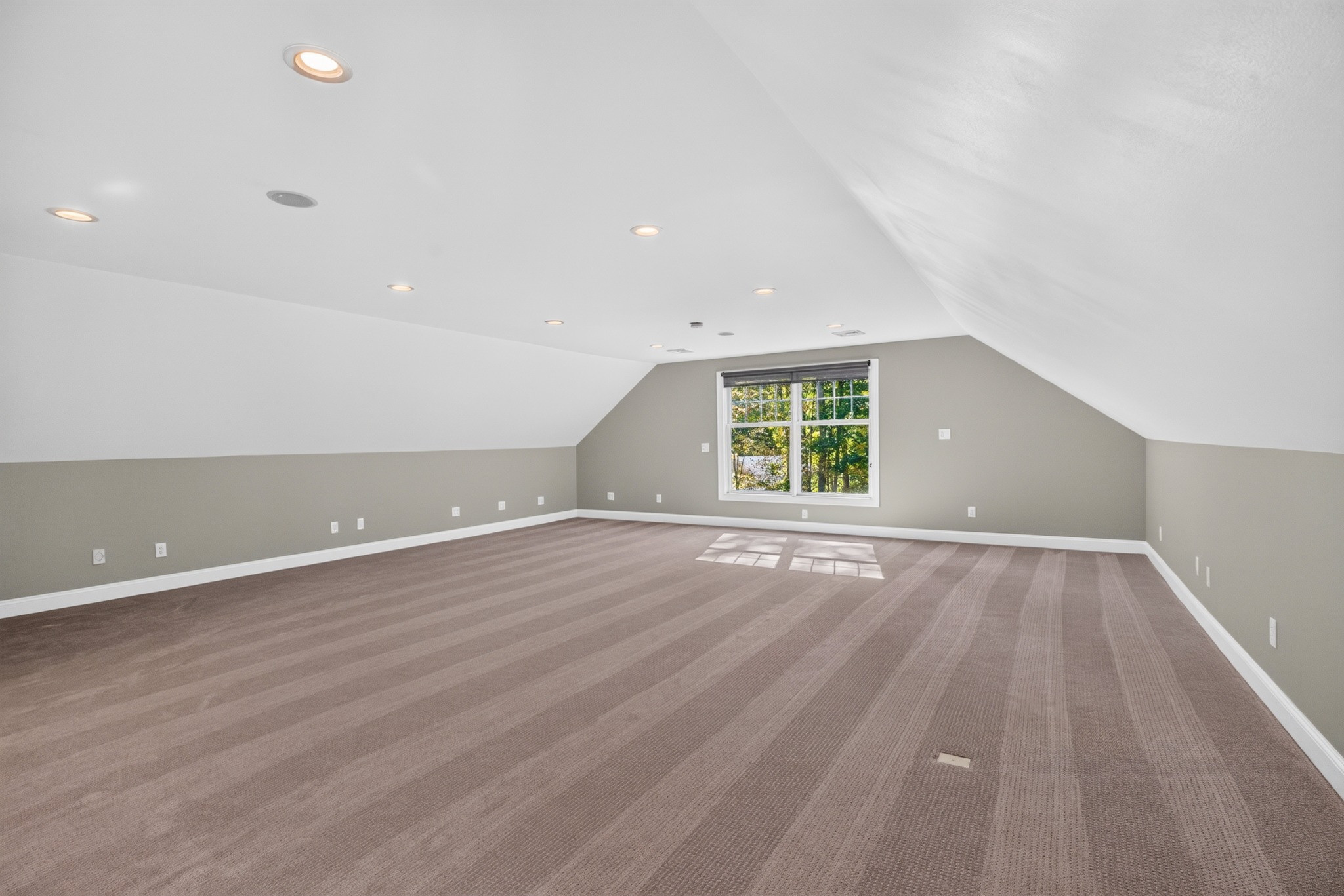 Open finished attic room with sloped ceilings, soft carpeting, and a sunny window.