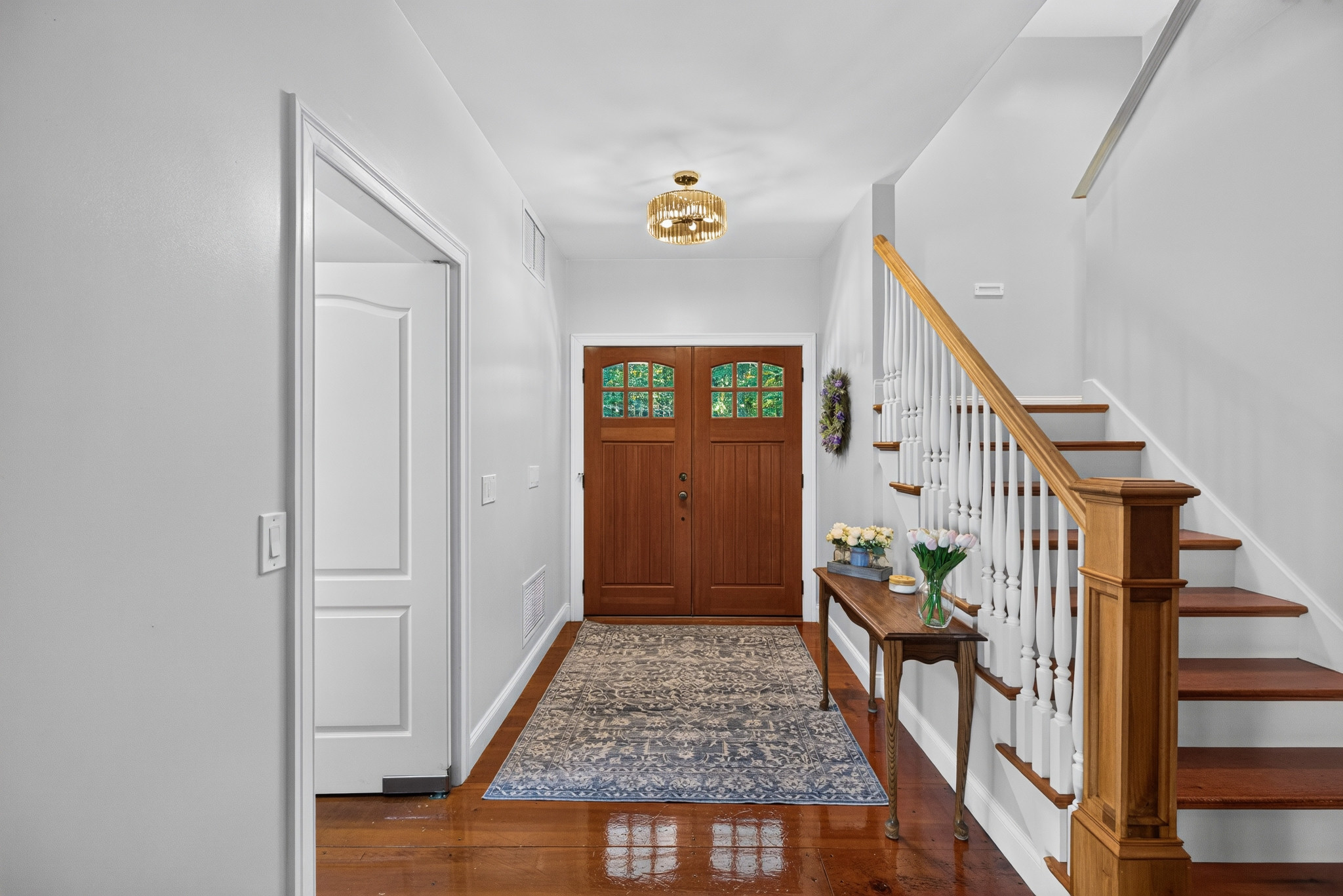 View along a light-filled entrance hall toward double wood doors and a staircase.