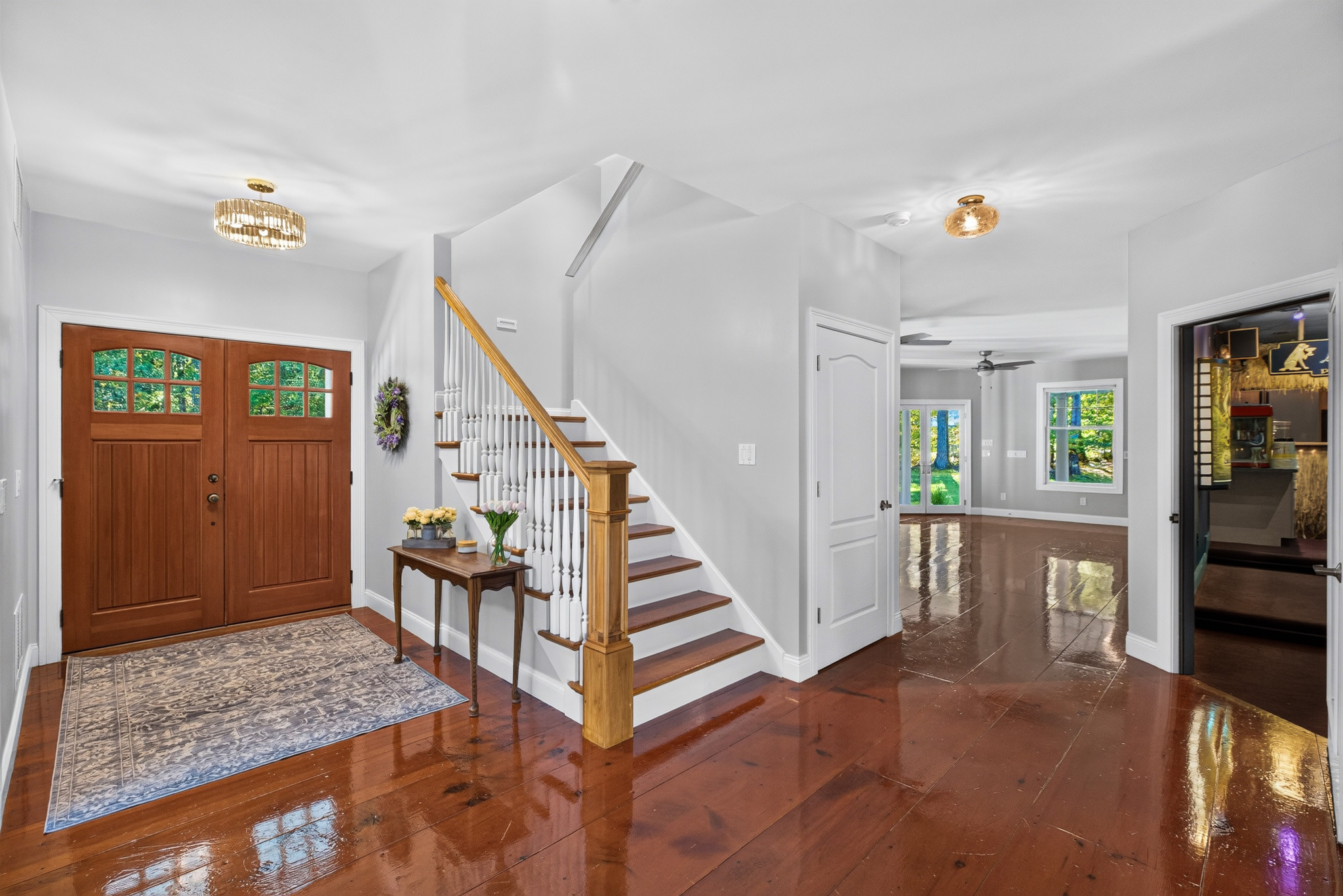 Wide foyer view with wooden stairs, double front doors, and adjoining spaces.