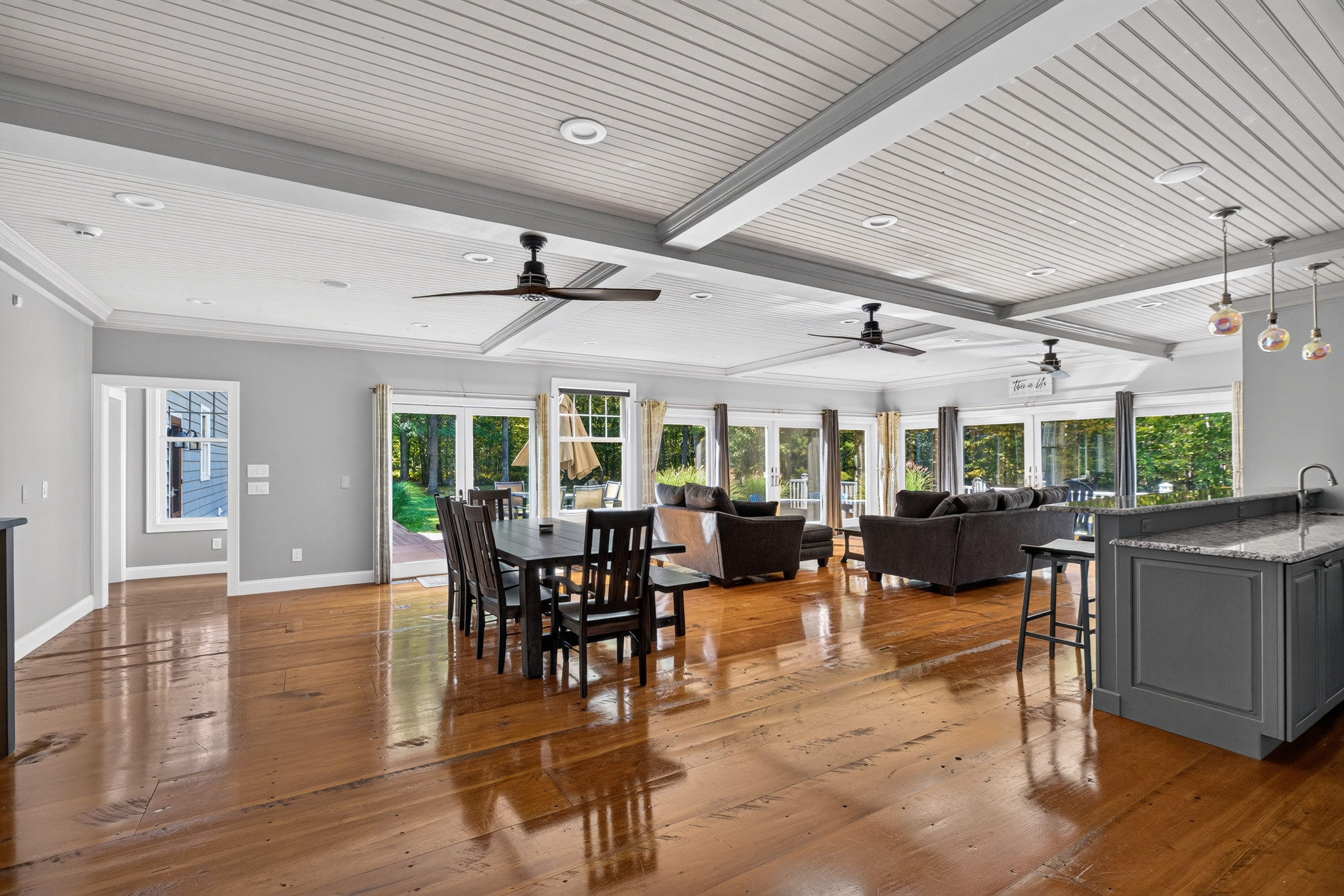 Open living and dining space with wood floors, ceiling fans, and broad windows.