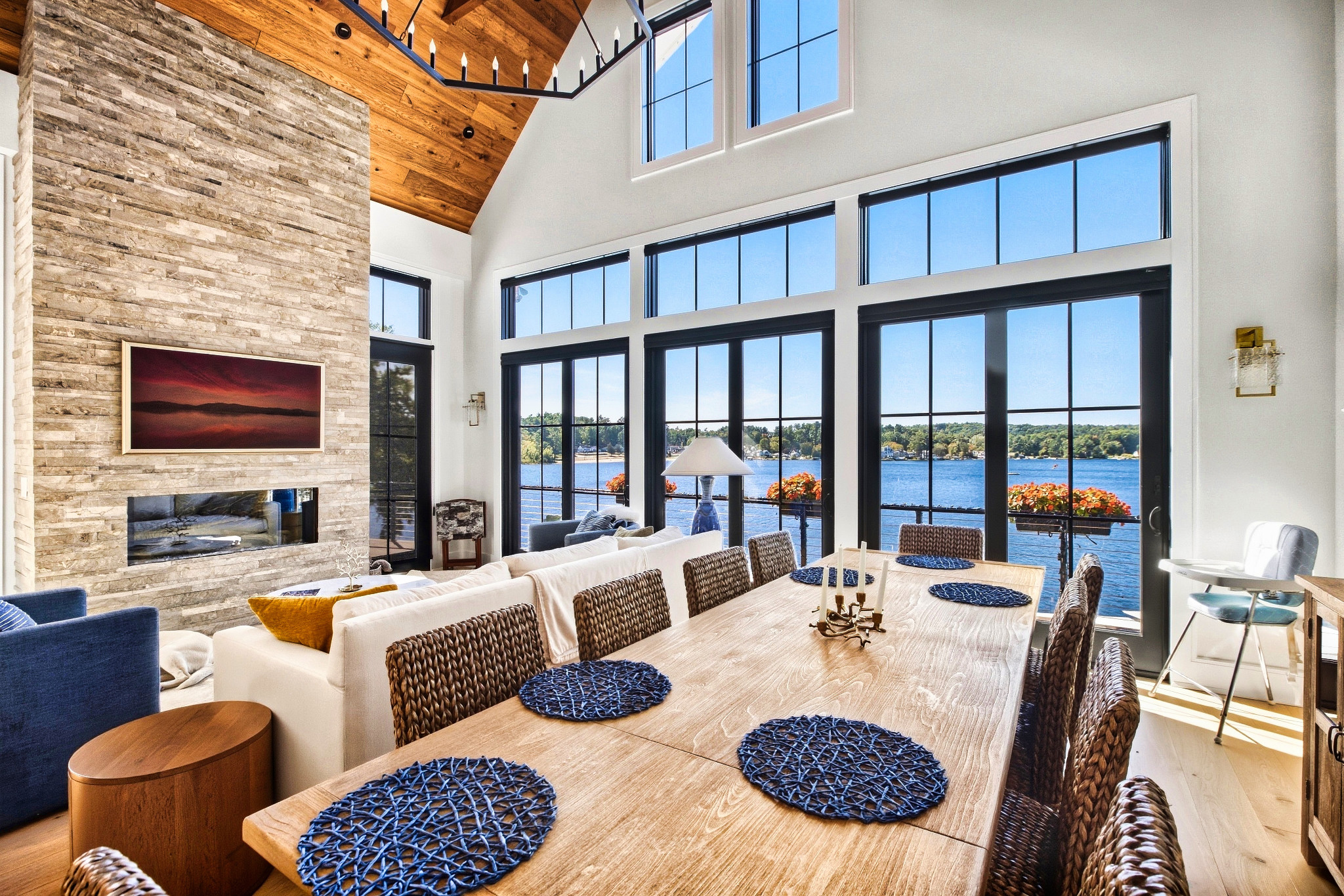 Tall windows frame a lake view beyond a dining and living space.
