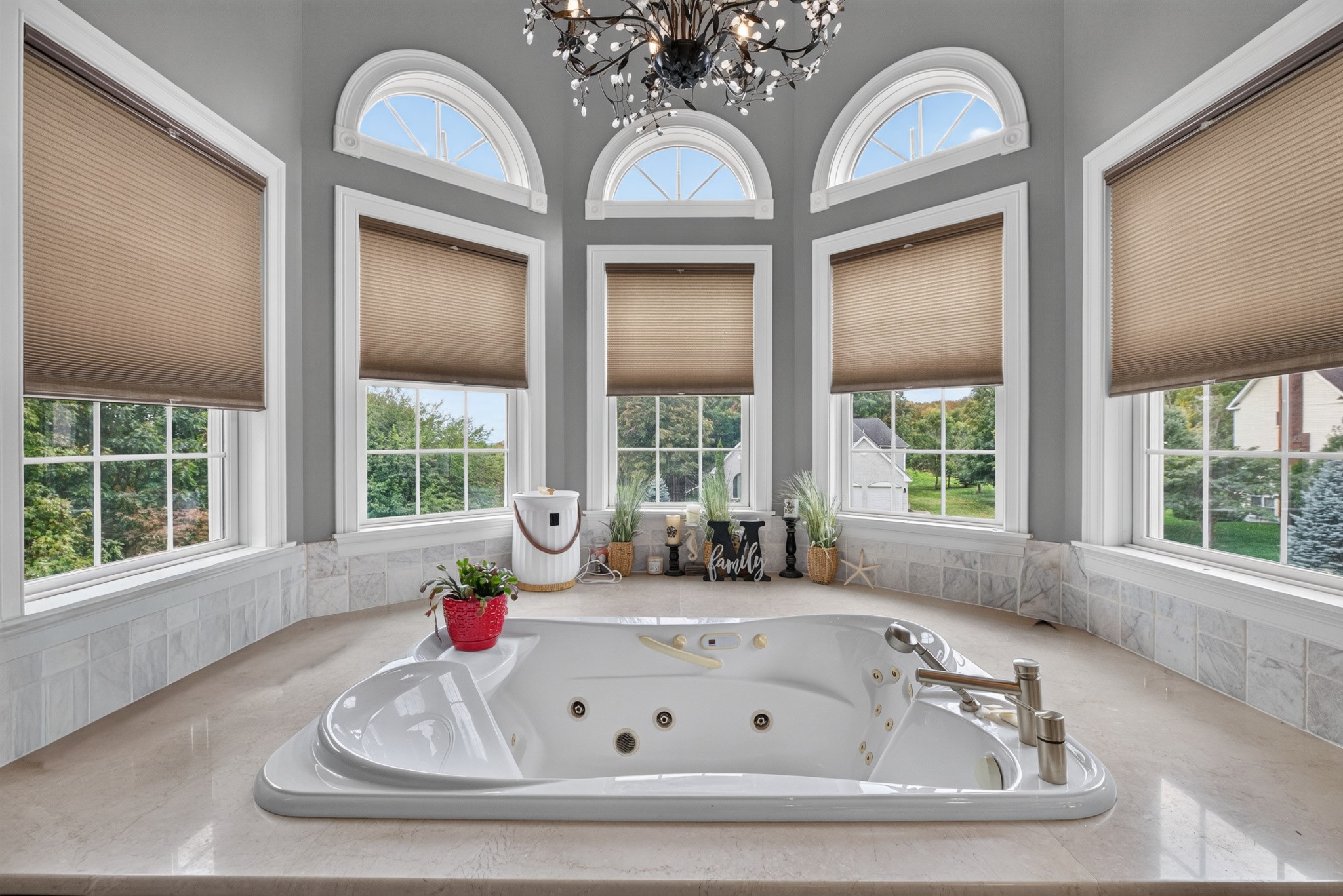 Spa bathtub beneath three tall arched windows and a chandelier.