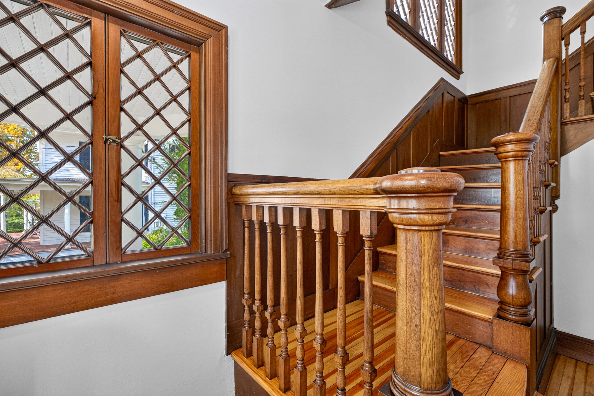 Crafted wooden staircase and newel post beside patterned glass windows.