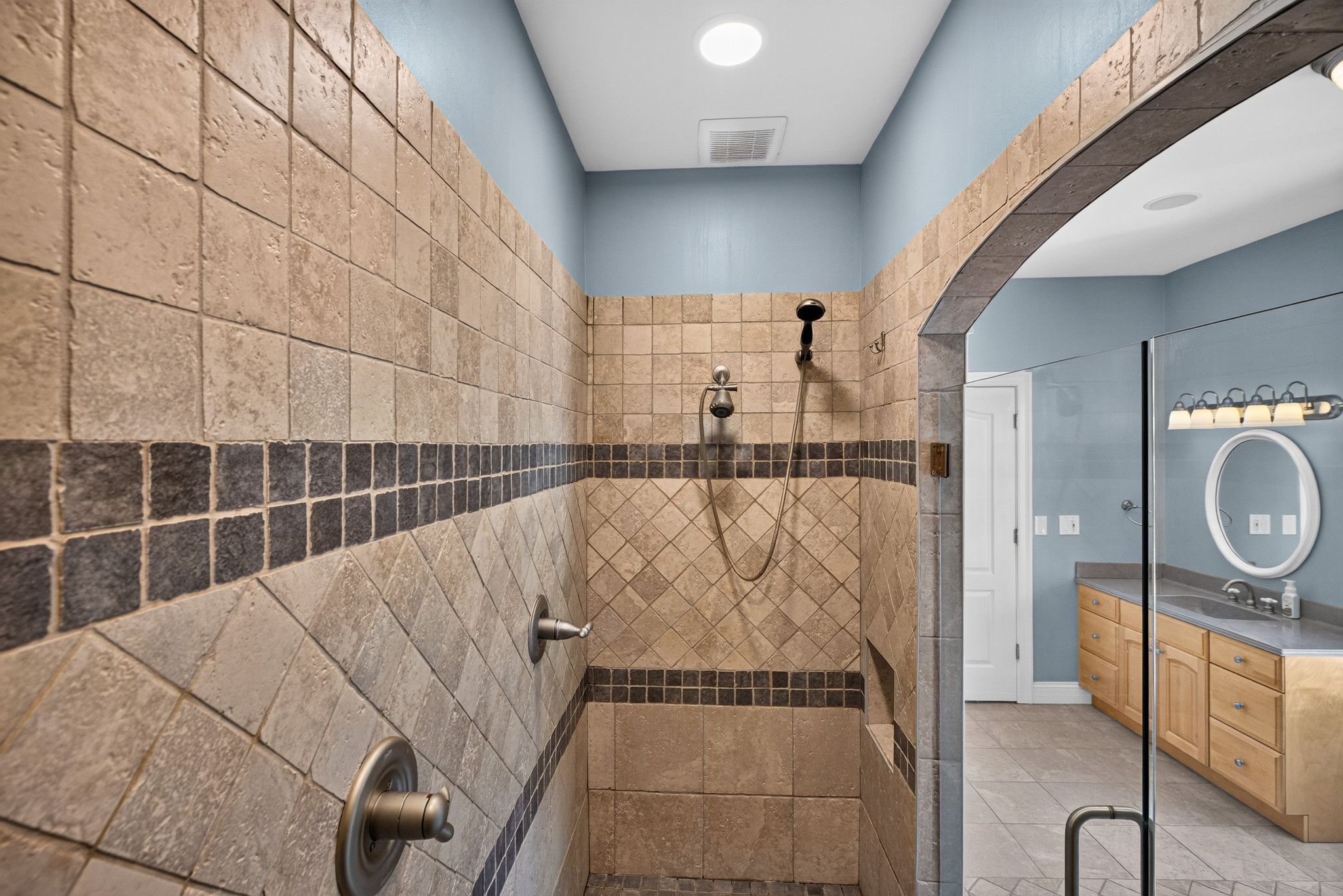 Tiled walk-in shower with an arched opening toward the vanity.