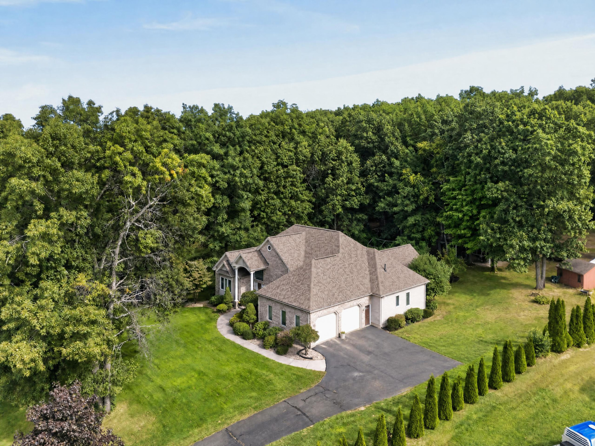 Aerial view of a house and driveway bordered by lawns and woodland.
